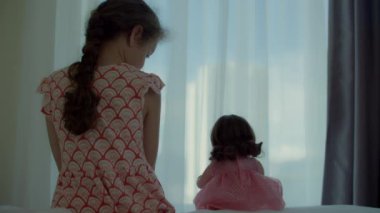 Çocuk kendine ve bebeğine koruyucu maskeler takıyor, yatakta oturup pencereden dışarı bakıyor. Ev karantinasında sıkılmış çocuk. Alerji, covid-19 koronavirüs salgını, salgını önleme.