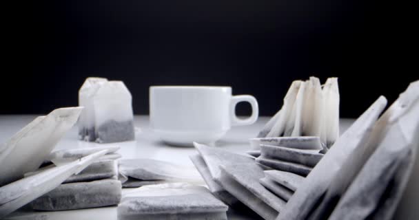 Super primer plano conjunto de bolsas de té en una mesa blanca sobre un fondo negro y una taza de té blanco.Hacer té de la mañana. Bolsas de té en una taza de té blanco — Vídeos de Stock