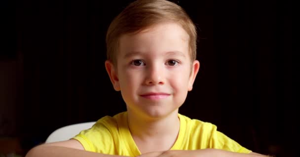 Portrait Drôle petit garçon souriant enfant regardant la caméra sont assis sur le fond noir, enfant mignon enfant avec joli visage. Concept d'une enfance heureuse. — Video