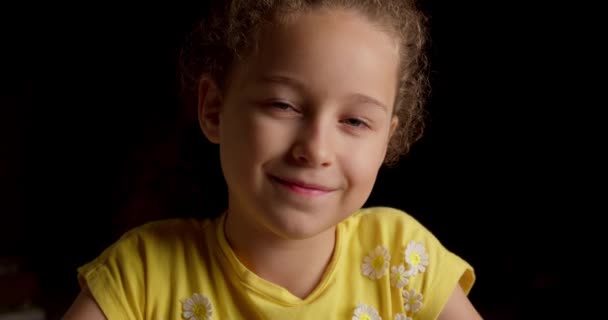 Portré Vicces kislány mosolygós gyermek néz kamera ülnek a fekete háttér, aranyos gyerek gyermek csinos arc. A boldog gyermekkor fogalma. — Stock videók