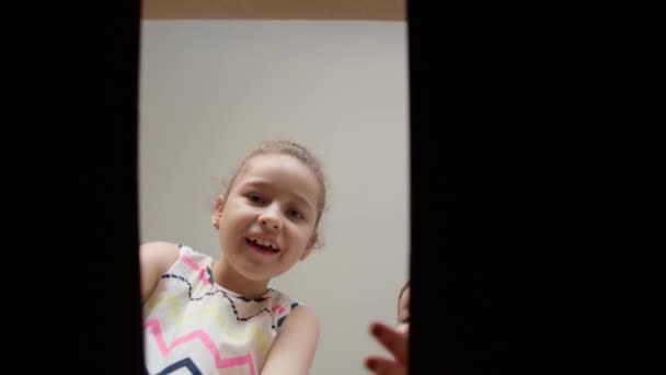 Niños felices, encantados con la sorpresa, abran una caja con regalos. Hijitos, una niña y un hermano, miren en una caja de cartón. Vista interior. Los niños meten sus manos en la caja. — Vídeos de Stock