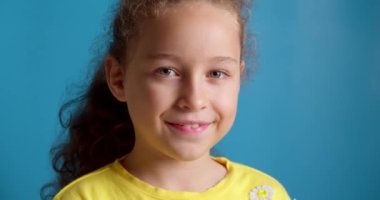 Gülümseyen mutlu bir çocuğun portresi, kameraya bakan küçük bir kız, gülümseyen, mavi arka planda bir çocuğun portresi, güzel yüzlü şirin bir çocuk. Mutlu çocukluk kavramı.