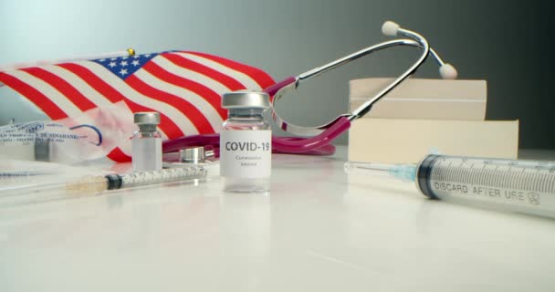 COVID-19 aşısı geliştirildi, koronavirüs aşısı ampulü ve çeşitli şırıngalar, tıbbi aletler, yüz kalkanı, Amerikan bayrağı geçmişi ve kitapları geliştirildi.. — Stok video