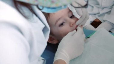 Kadın dişçi klinikteki küçük bir çocuğun bebek dişlerini muayene ediyor. Kadın profesyonel dişçi iş başında. Diş muayenesi kavramı.