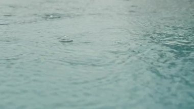 Büyük su birikintisinin üzerine yağmur damlaları, güçlü dalgalar, yağmur damlaları, yavaş çekimde yakın çekim. Yağmur suya yağar. Sel yağmurlu mevsimdir ve şiddetli yağmurdur..