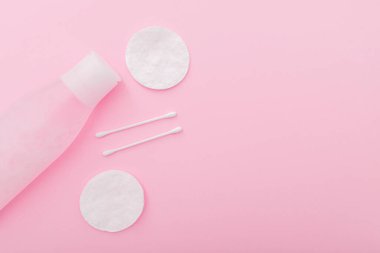 Plastik şişede losyon, pamuk pedler ve pembe arka planda çubuklar ile basit kompozisyon, üst görünüm, yatar