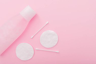 Plastik şişede losyon, pamuk pedler ve pembe arka planda çubuklar ile basit kompozisyon, üst görünüm, yatar