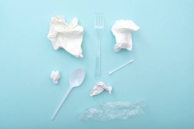 Kullanılan plastik tabaklar çöp, buruşmuş kağıt peçeteler, pamuk tomurcukları, kaşık, çatal, mavi arka planda plastik paket, konsept