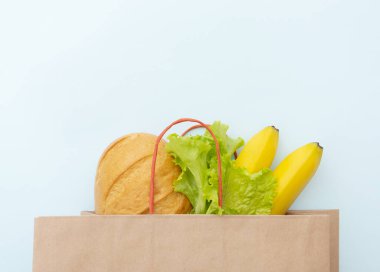 Yiyecek dolu kağıt poşet: yeşil salata, ekmek ve muz yaprakları. Mavi arka plan, üst görünüm üzerine uzan