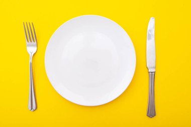 Sarı yüzey üzerinde çatal ve bıçak olan seramik beyaz tabak, mutfak masası, üst görünüm, metin için boşluk
