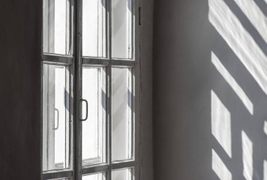 Duvarında pencere, çerçeve, güneş ışığı ve gölgeler olan odanın içi