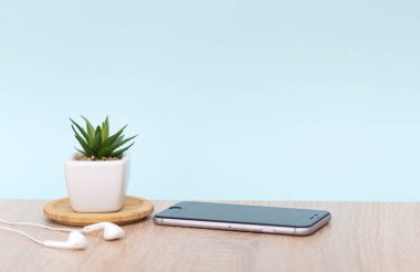Ofis, cep telefonu, kulaklık, ev bitkisi olan bir masa. Mavi duvarlı, kahverengi masalı. Resim kavramı.