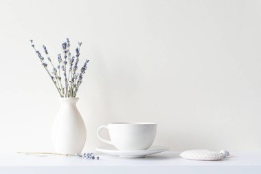 Minimum kompozisyonda yaşam, lavantalı kurutulmuş buket, seramik beyaz bardak ve sıcak içecek çayı veya kahve, bej tonda sabah havası 