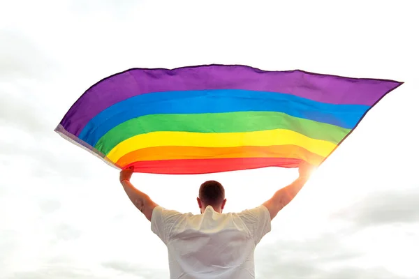 Rüzgarda sallanan gökkuşağı gay bayrağı tutan gururlu adam, insan hakları ve eşitlik konsepti
