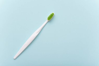 Düz olarak yeşil kıllı beyaz plastik diş fırçası. Mavi yüzeyde diş fırçası, üst görünüm, metin için boşluk. 