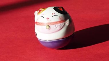 Maneki-neko kedisi, kırmızı arka planda seramik biblo. Japon heykelciğinin sahibine şans getirdiğine inanılır, 4K.