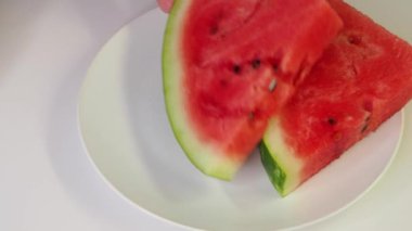 Beyaz tabağa olgun kırmızı karpuz dilimleri koyan bir adam. Seramik tabağın üzerinde karpuz dilimleri olan piknik. Video 4k çözünürlüğü.