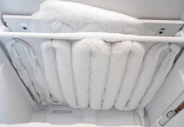 Close-up of opened deep freezer with ice and snow. Freezer before defrost. Empty shelves of fridge.