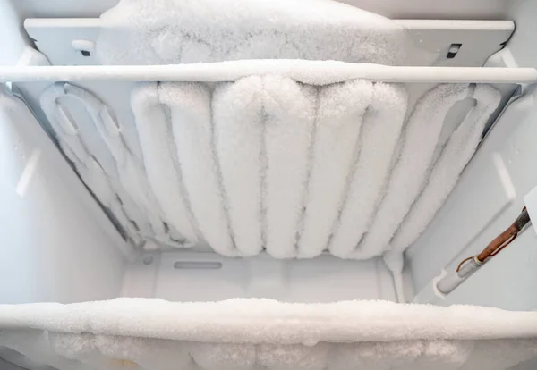 Close-up of opened deep freezer with ice and snow. Freezer before defrost. Empty shelves of fridge.