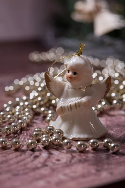 Ceramic angel and golden, shiny christmas chain lying on the wood table — Stock Photo, Image