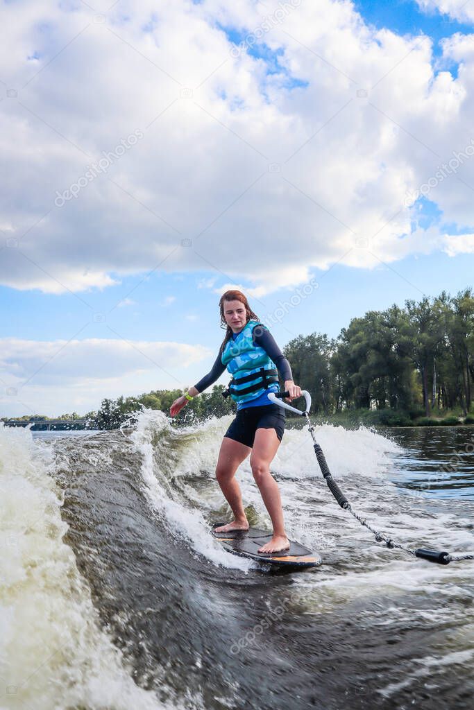 The girl is learning to ride a wakesurf on the river behind the boat. Wake vest. Board