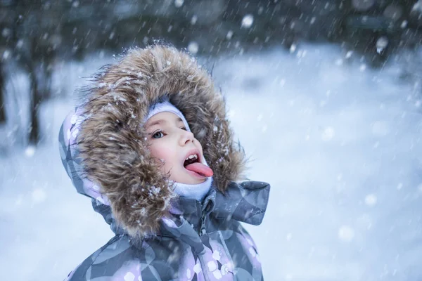 Πορτρέτο ενός χαριτωμένου μικρού κοριτσιού που πιάνει νιφάδες χιονιού στο στόμα τη μέρα του χειμώνα — Φωτογραφία Αρχείου