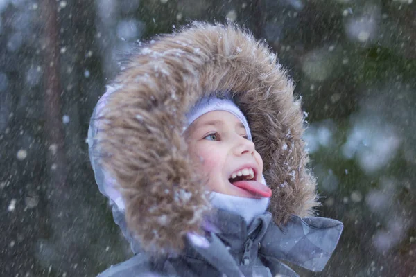 Portrait d'une jolie petite fille qui attrape des flocons de neige bouche dans la journée d'hiver Photo De Stock