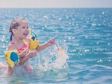 Bir çocuk kolluklarıyla denize su sıçratıyor.