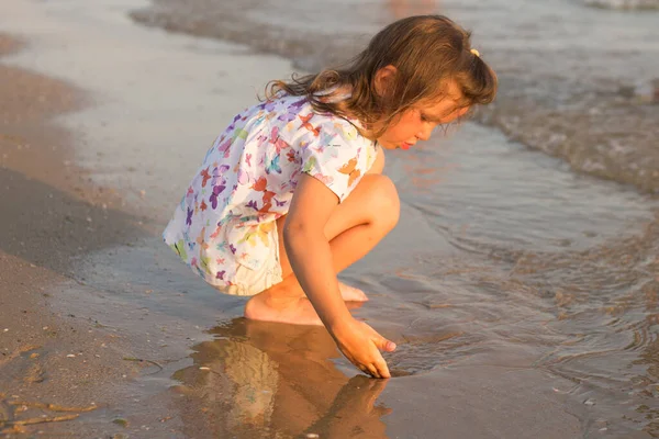 La piccola ragazza carina seduta e che gioca sulla spiaggia — Foto Stock