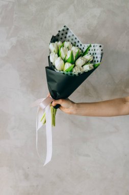 A bouquet of white tulips in black packaging with polka dots in the hands of a girl. Summer background