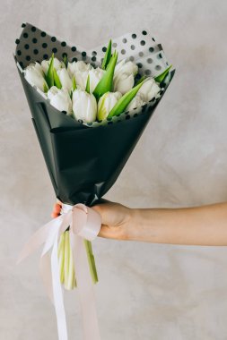 A bouquet of white tulips in black packaging with polka dots in the hands of a girl. Summer background