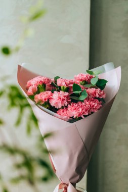 Delicate bouquet of coral carnations with eucalyptus greens with green bokeh. Summer background