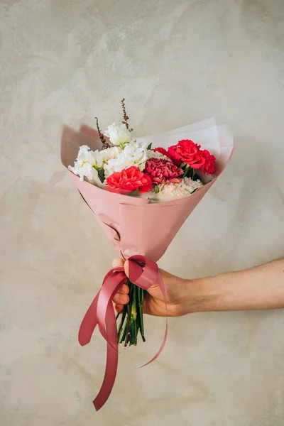 Bright summer bouquet of red roses, burgundy and white carnations, white eustomas in pink packaging. Summer background