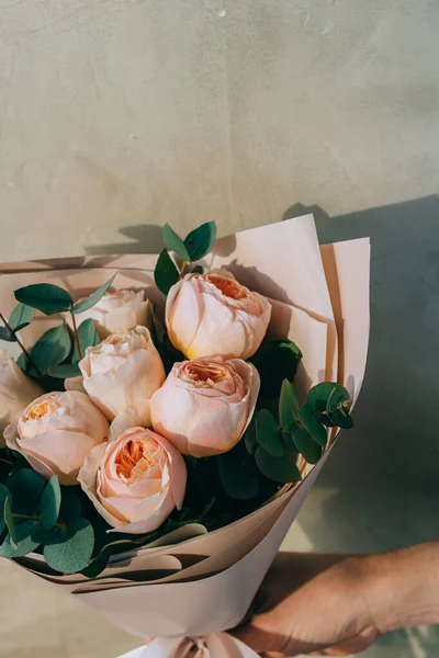 Bouquet of delicate peony roses of peach color with eucalyptus in a paper package. Summer background.