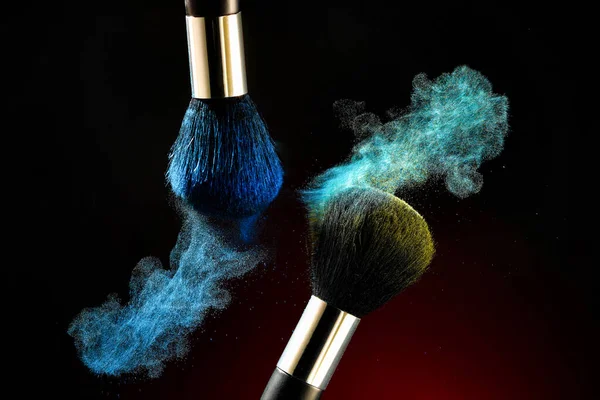 Perfect splash after touching two professional brushes with powder particles on the tip of blue and yellow colors on a black background, close-up. Makeup brushes