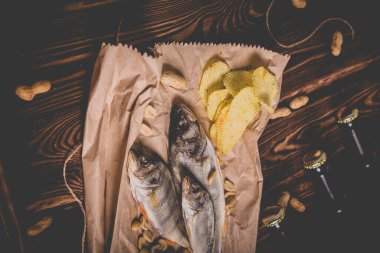 Kahverengi cam bira şişeleri ve kurutulmuş balık, cips, fındık ve tahta arka planda kraker. Stüdyo fotoğrafı.