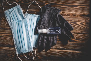 Tıbbi maskeler, siyah lastik eldivenler ve ahşap arka planda şeffaf bir dezenfektan. Covid-19 virüs koruma tıbbi konsepti. Vignetting ile Stüdyo fotoğrafı.