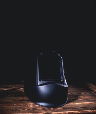 Ahşap bir arka planda siyah kaynak maskesi. Sert ışıklandırmalı bir stüdyo fotoğrafı..