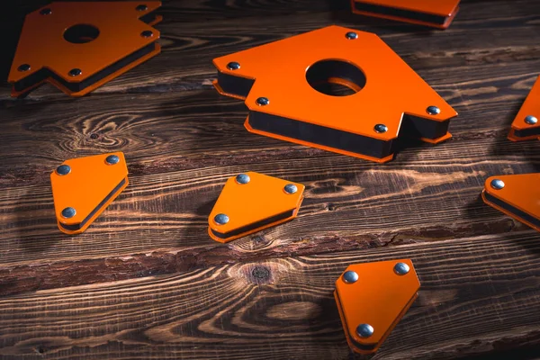 固定角度値の金属構造物を溶接するためのオレンジ色の磁気コーナーのセット 木製の背景に硬質照明付きのスタジオ写真 — ストック写真