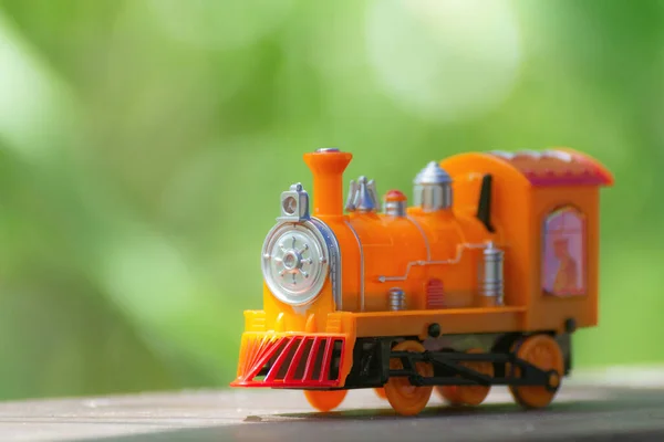 Orange toy train parked on a wooden floor with bokeh playing distance.