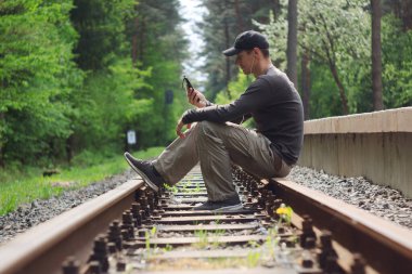 Adam ormanda bir tren yolunda oturur ve müzik dinler..
