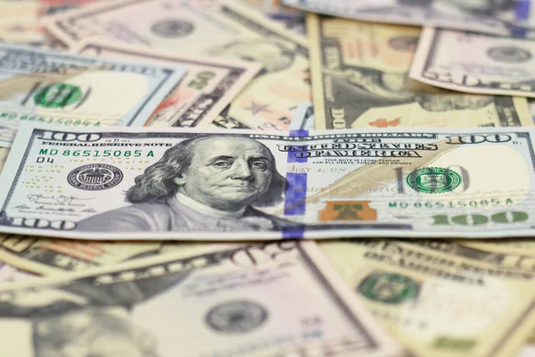 100 dolarlık banknot, farklı değerlerde, bulanık arka planda dağınık dolar banknotlarının üzerinde yatıyor.