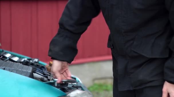 Un hombre vestido de negro desenrosca los pernos del faro del coche — Vídeos de Stock