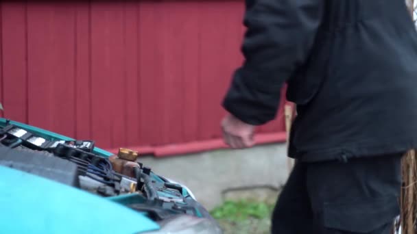 Человек в черной одежде подходит к открытому капоту машины и убирает инструменты — стоковое видео