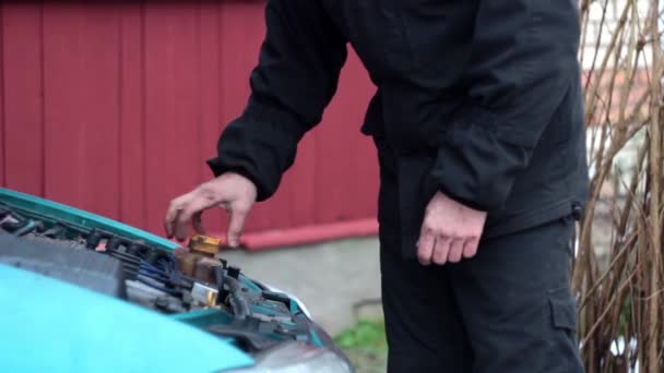 Ein Mann in schwarzer Kleidung schraubt den Deckel des Tanks der Kühlanlage des Autos ab und zieht den Deckel fest — Stockvideo