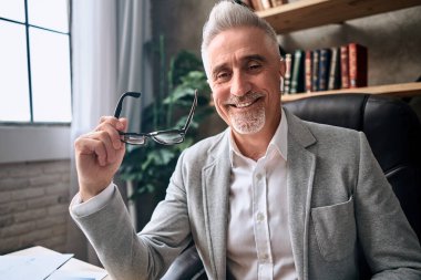 Gri ceketli, gri ceketli, iş yerinde kameraya bakan mutlu sakallı iş adamının portresi. İş konsepti