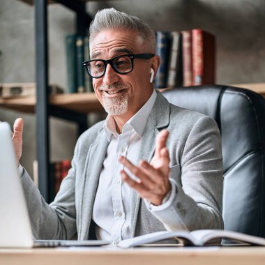 Ofiste dizüstü bilgisayarla konuşurken kablosuz kulaklıkla gülümseyen yetişkin iş adamının portresi. İş konsepti