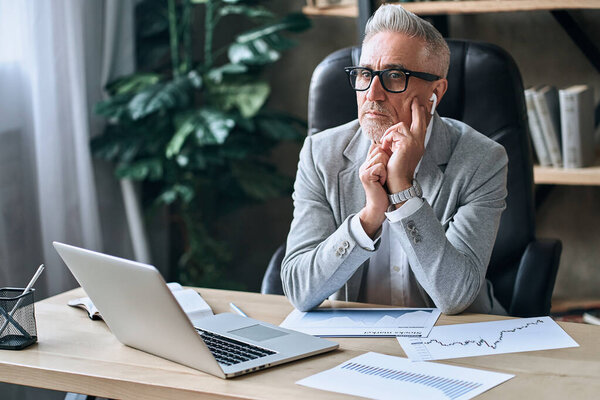 Adult businessman in stylish clothes sitting at his desk in the office while thinking about further tasks in work. Business career concept