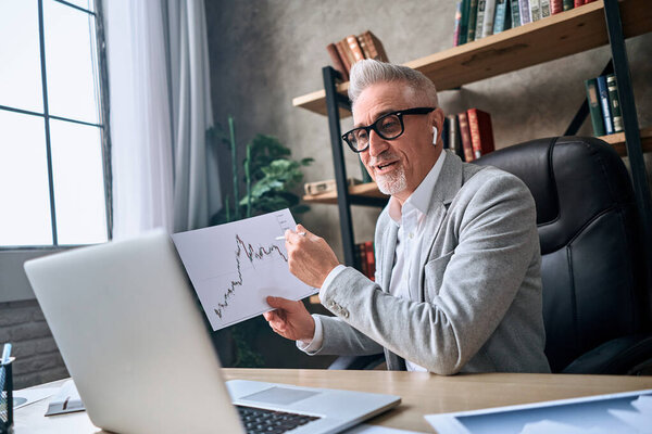 Happy mature man having online meeting with colleagues and discussing the data on the report in his office. Business concept