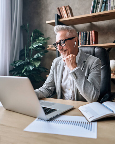 Happy mature man enjoying working day while using laptop and looking at screen in the office. Business concept